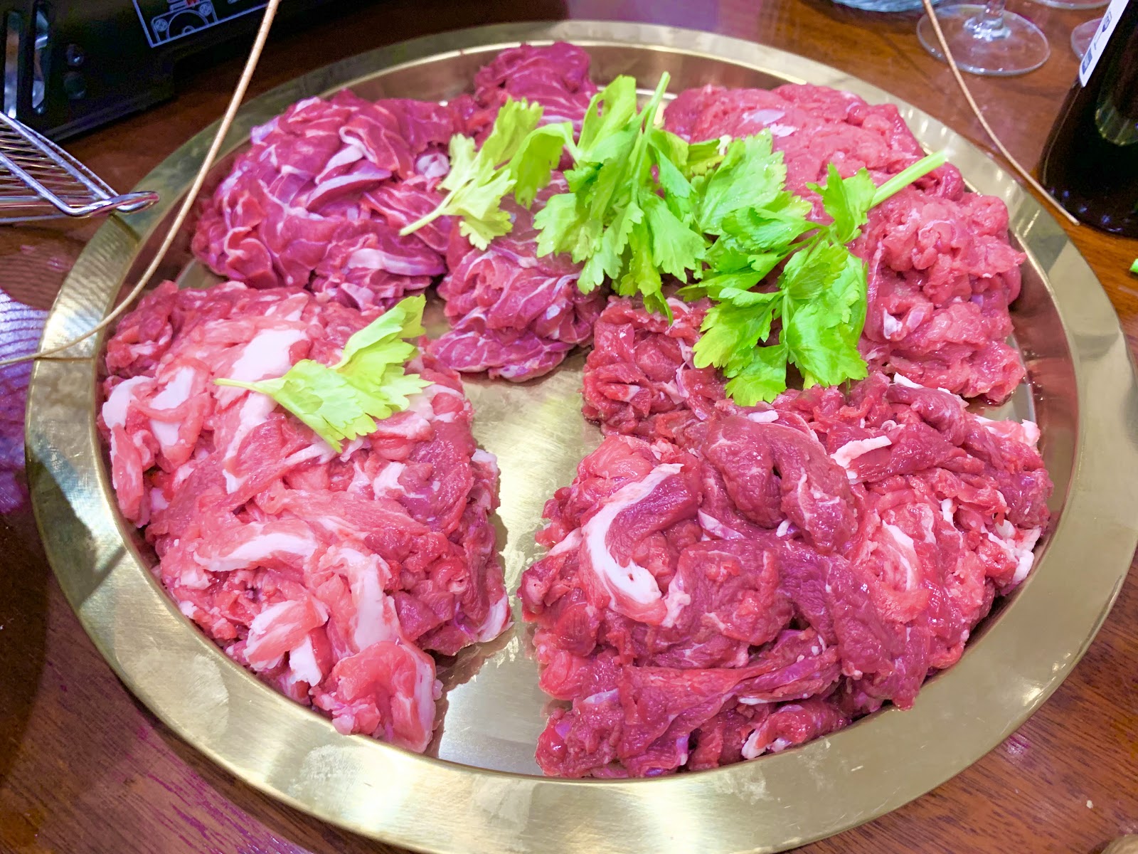 A round gold tray of raw sliced beef topped with coriander