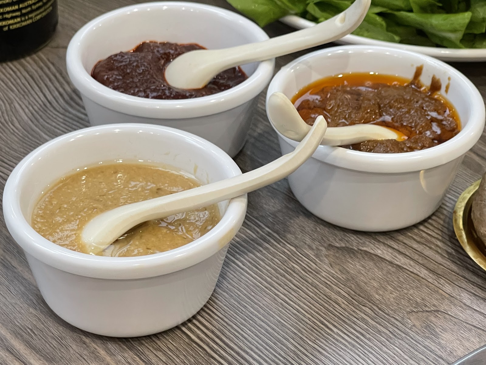 Three small tubs of dipping sauce with ceramic spoons