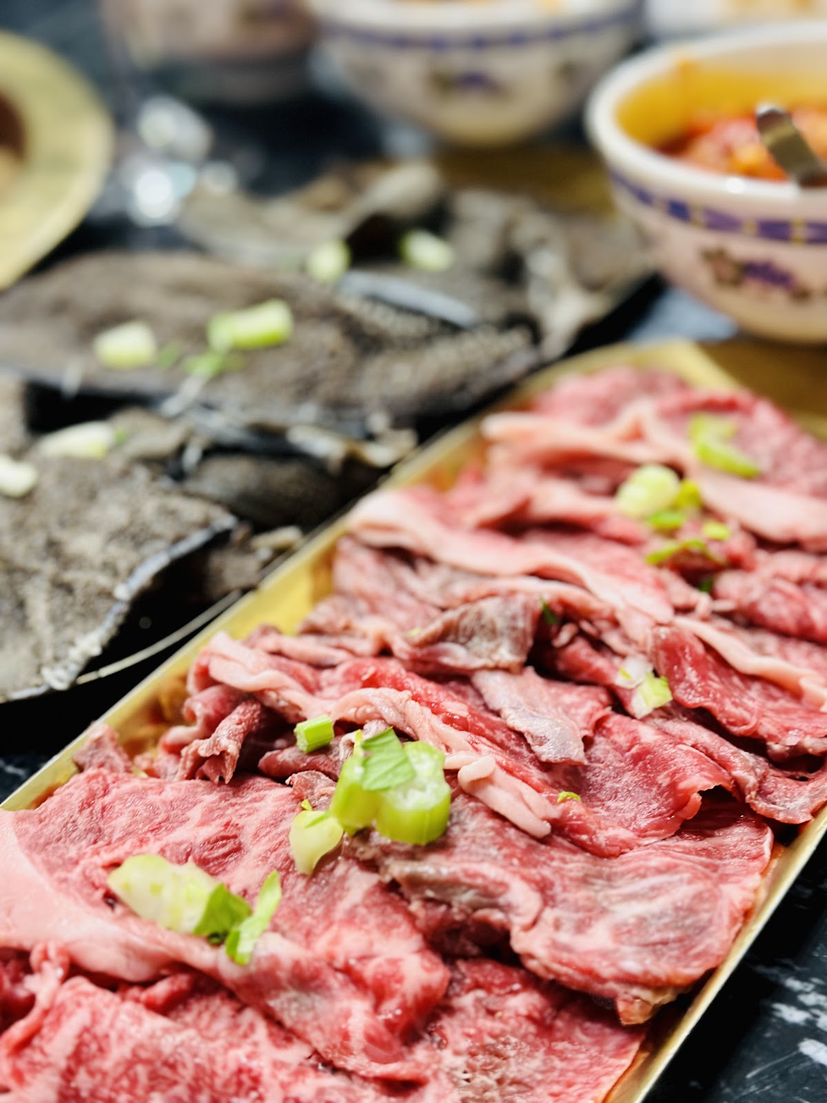 Close-up of marbled sliced beef on a gold tray with spring onion